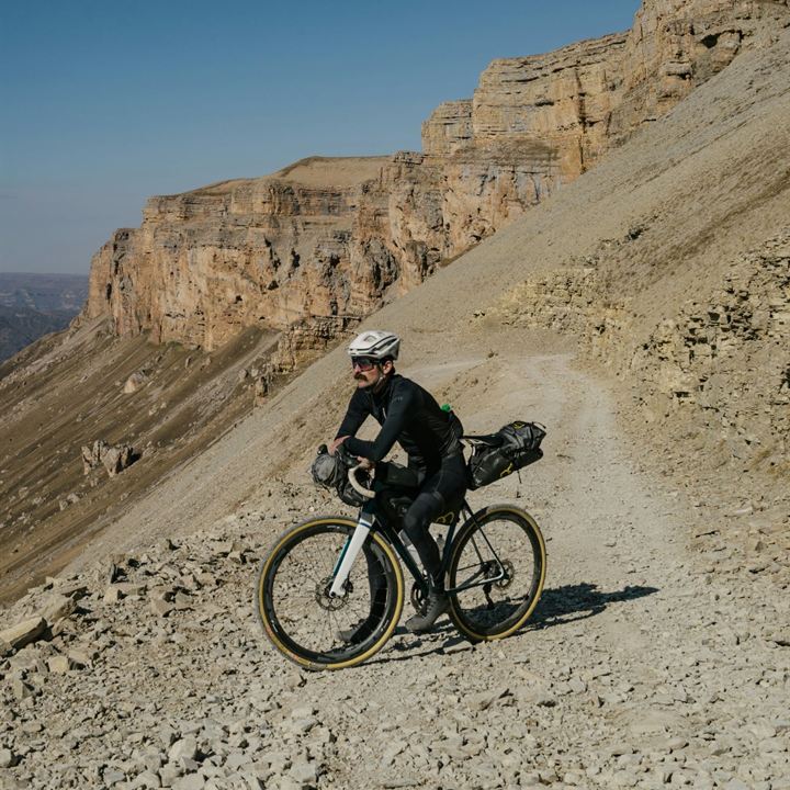 A bikepacker on a gravel road below a limestone cliff