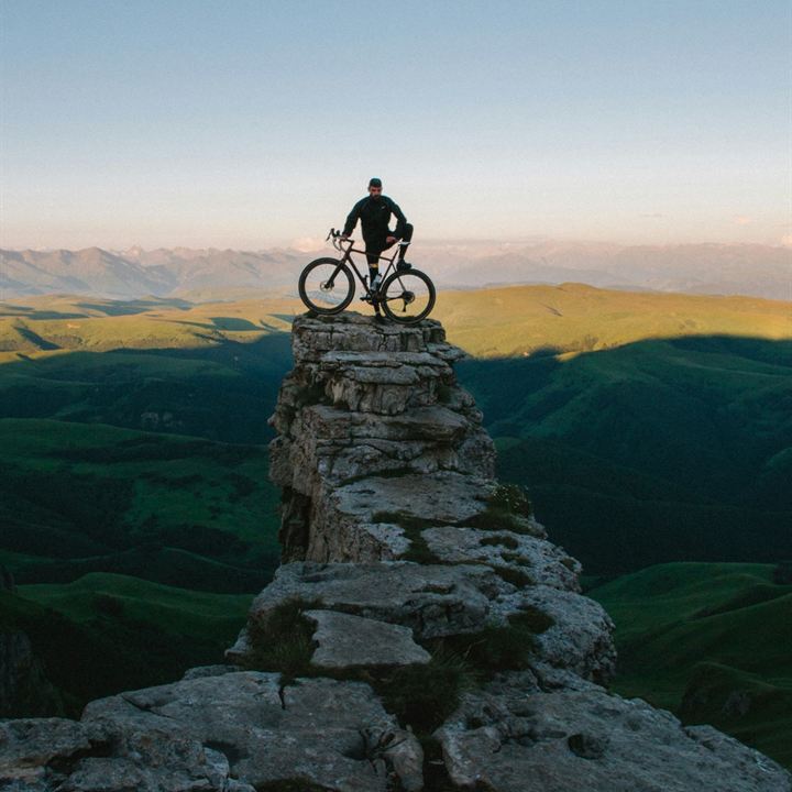 A cyclist standing with a gravel bike on top of a rock pillar